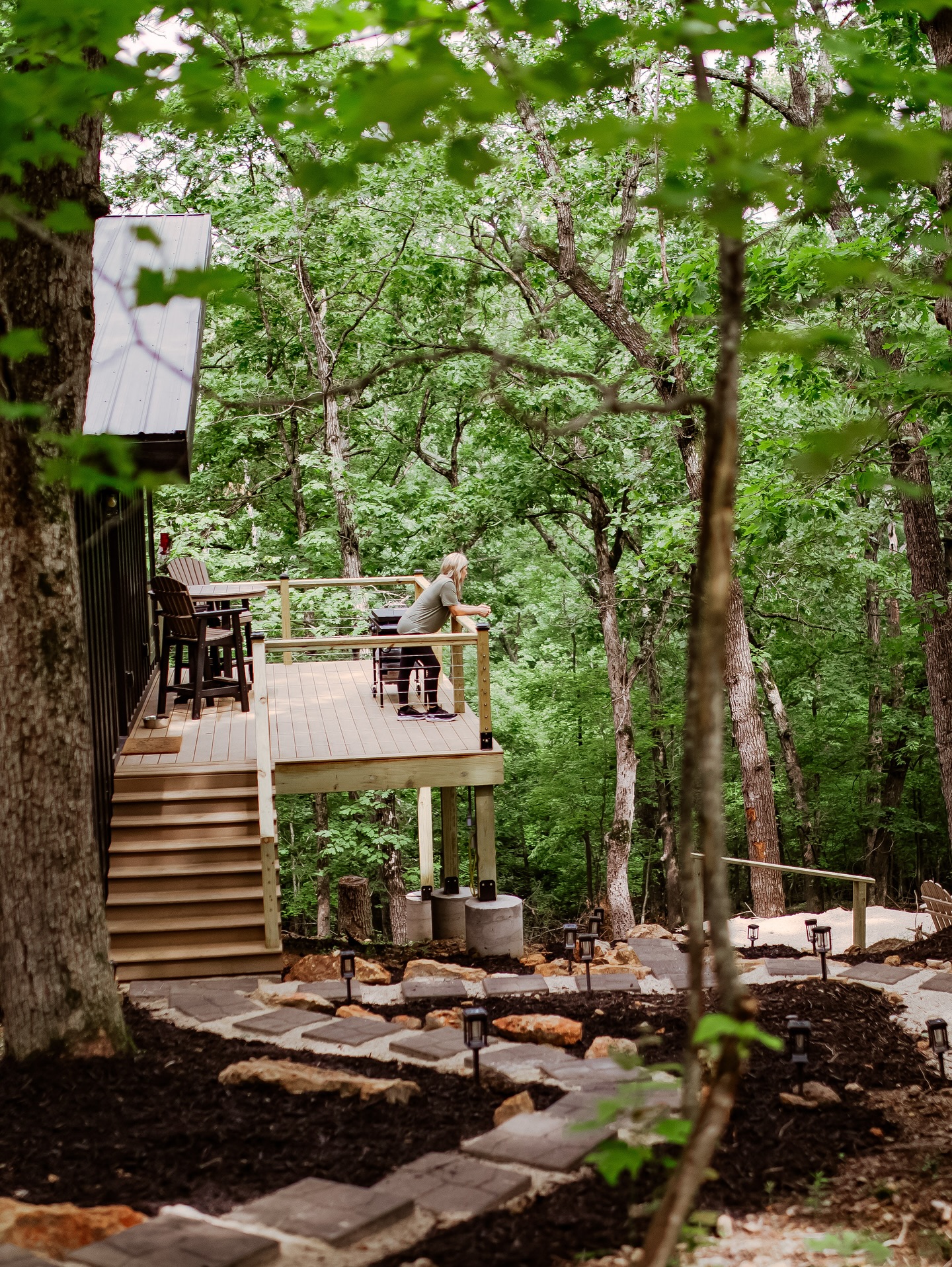 Wooden deck overlooking lush forest with stone pathway and garden lights